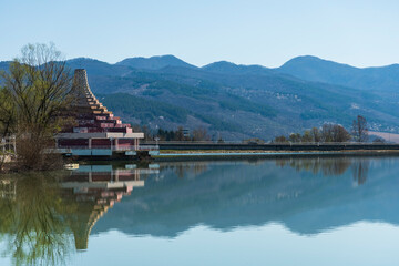Fototapeta na wymiar A pyramid like building on the coast of a lake in Bulgaria. Famous attraction. Mountains in the distance. Sunny day.