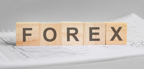 FOREX is written on light wooden blocks. the word is located on a sheet with charts and graphs