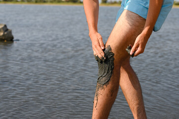 The man of the lake smears his knee with black medicinal mud from salty. Alternative medicine for...
