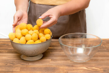 Caucasian woman chef peeling apricots fruits in bowl, preparing for making jam at home kitchen at summer autumn, online cooking, recipe instruction