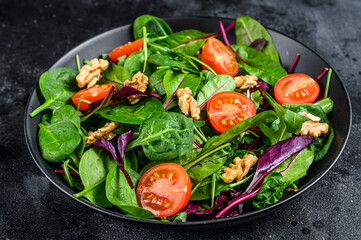 Vegetarian salad with mix leaves mangold, swiss chard, spinach, arugula and nuts in a salad bowl. Black background. Top view