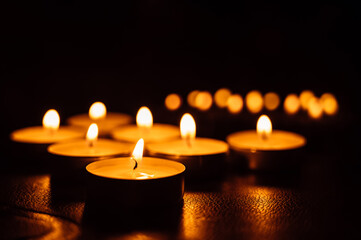 Close-up of burning tea candles in the dark. Reflection of candlelight flame.