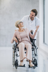 Fototapeta na wymiar Doctor Pushing His Senior Female Patient In A Wheelchair Along The Hospital Hallway