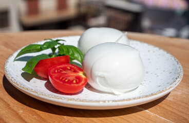 Cheese collection, white balls of Italian soft cheese mozzarella served on outdoor terrace with fresh tomatoes and basil with Italian houses on background