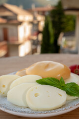 Cheese collection, variety of Italian cow milk cheese flat scamorza with Italian houses on background