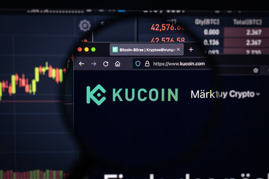 Kucoin crypto exchange  logo on a website with blurry stock market developments in the background, seen on a computer screen through a magnifying glass