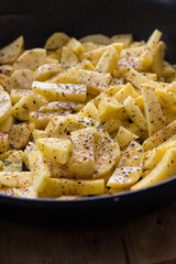 Closeup view of a cast iron pan with a lot of raw spicy potatoes inside.