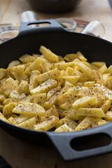 Closeup view of a two handles cast iron pan with a lot of raw spicy potatoes inside.