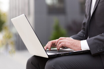 Close-up photo of a male businessman's hand in a business suit working on a white laptop