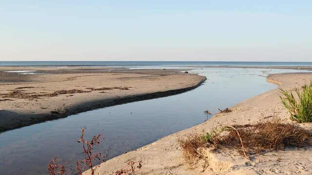 River flowing calmly and slowly to the sandy Baltic sea coastline and forming a delta with some shallow ponds at the mouth of the river and sea meeting point on a sunny afternoon