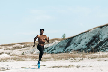 Naklejka na ściany i meble Full length, healthy African American man, muscular man running outdoors in mountains