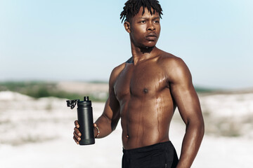 Portrait African American man, fitness athlete, with a bottle of water after training on a sunny...