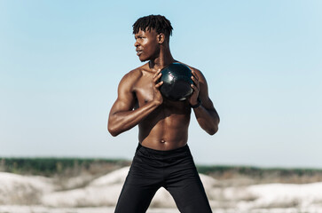 African American crossfit man, fitness man holding abdominal workout ball, outdoors - Powered by Adobe