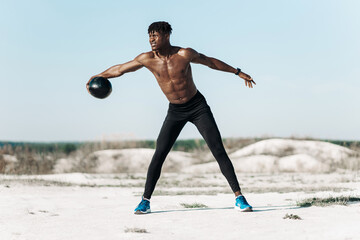 Fitness African American man doing workout twist exercise with medicine ball weight, outdoors on nature