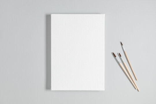 Blank white canvas mockup and paint brushes on gray background. Flat lay, top view, copy space