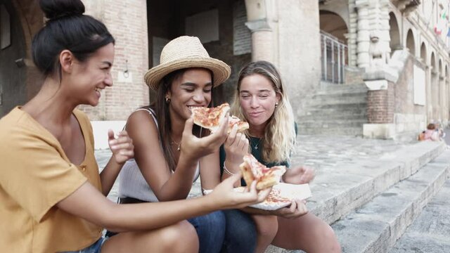 Three cheerful multiracial women eating pizza in the street - Young people lifestyle and summer vacation concept