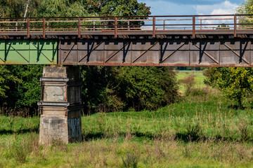 an old rusty railway bridge on a green meadow with trees in autumn colors in the background
