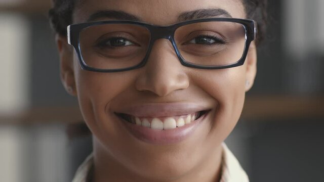 Close up portrait of young positive african american lady in eyeglasses smiling to camera, slow motion