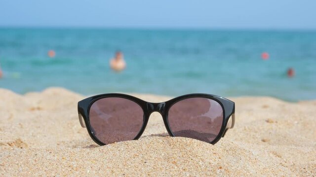 Closeup of black protective sunglasses on sandy beach at tropical seaside on warm sunny day. Summer vacation concept.