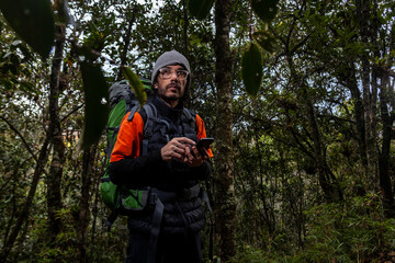 Man on an adventure trip through a forest with dry leaves floor of Colombia, next to her a green backpack