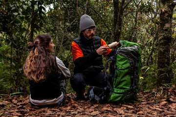 Couple on an adventure trip through a forest with dry leaves floor of Colombia, next to them a green backpack