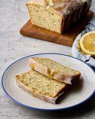 Vertical of sliced lemon bread on plate. Delicious citrus cake with poppy seeds and white frosting. Traditional vegetarian homemade fruit pie. Loaf of orange bakery on background