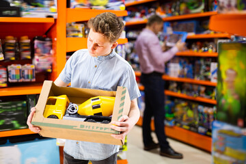 Focused teenage boy choosing toy cement mixer machine in modern toy store