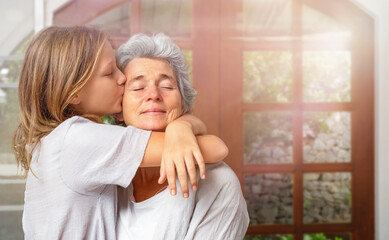 Teenager girl hugs and kisses senior woman indoor