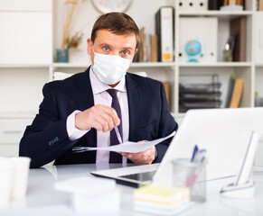 Businessman in medical face mask conducting meeting in office. Concept of social distance in work during coronavirus pandemic..