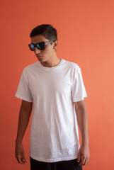 Young man standing wearing white plain t shirt and sunglasses. Orange wall in the background