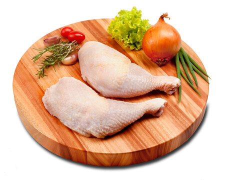 Coxa e sobrecoxa do frango crua, sobre tábua de madeira redonda no fundo branco para recorte.