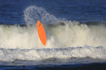 bright orange surfboard coming out of a wave by itself 