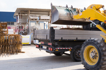 Yellow excavator moving sand to empty truck at hardware store warehouse on a sunny day