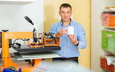 Man uses machine to print on ceramic mug. High quality photo