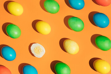 A pattern of Easter multicolored eggs on a bright orange background with one peeled egg. The spring composition of Easter. Minimal flat lay.