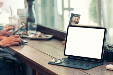 Blank screen tablet with magic keyboard on wooden counter table in cafe room.