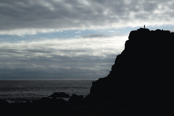 piedra junto a la silueta de un sujeto y el mar de fondo en contraluz