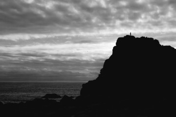 piedra junto a la silueta de un sujeto y el mar de fondo en contraluz en blanco y negro