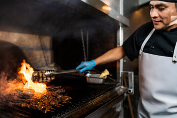 Cook holding a piece of meat with a pair of tongs in the grill