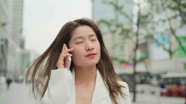 slow motion Confident Asian businesswoman in white suit talking on the phone walking in the uran city street at Chengdu China