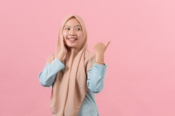 Asian muslim woman smiling and pointing to presenting something on her side with copy space