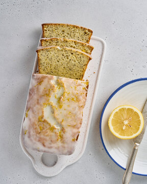 Flat lay of sliced lemon bread with poppy seeds, white frosting and citrus peel. Tasty sweet fruitcake on cutting board. Healthy dessert recipe. Delicious orange bakery. Top view, vertical