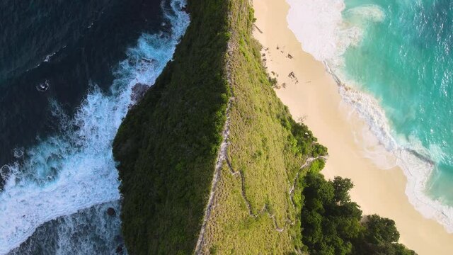 The high cliff between two tropical beaches at Kelingking Beach. Drone top down. Flying down.