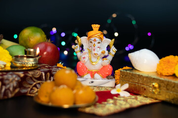 Colorful Statue Of Hindu God Ganesha Ganpati Bappa Morya Sitting On Golden Asana With Fruits, Flowers, Lamp And Blur Bokeh For Diwali Puja New Year Deepawali Ganesh Chaturthi Or Shubh Deepavali Pooja