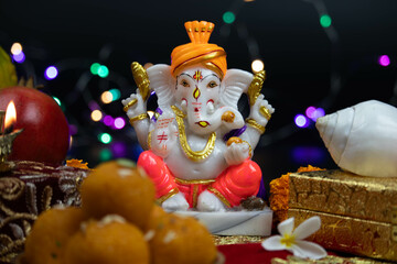 Hindu God Lord Ganesha Ganpati Bappa Morya In Orange Pagdi For Worship On Diwali Puja New Year Deepawali Ganesh Chaturthi Or Shubh Deepavali Pooja. Laddu Sweet Ladoo And Shankh in Blur With Bokeh