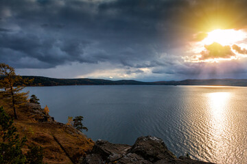 Beautiful lake and rocky shore in the rays of evening sun of golden autumn in cloudy weather