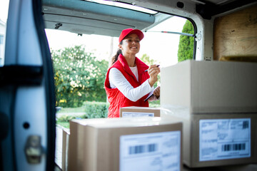 Portrait of hardworking female courier arranging packages before delivery. - obrazy, fototapety, plakaty