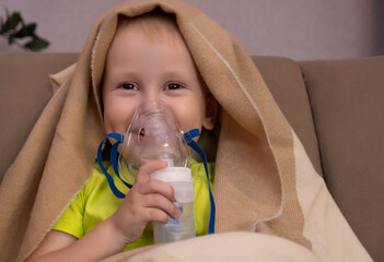 The baby sits on the couch, is treated with a nebulizer, the boy does inhalations, treatment at...
