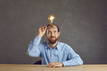 Man freelancer with light bulb over head sitting at table share bright idea or advanced solution studio shot on grey wall copy space. Startup project development, creativity and innovation concept