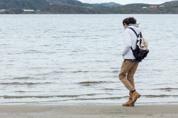 Young male traveler on the North Sea coast. A guy in a white jacket in a backpack. Freedom and relaxation. Space for text.